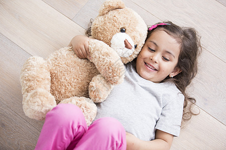 带着泰迪熊的女孩躺家里的木地板上图片