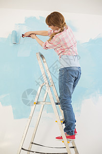 梯子上的女人用油漆滚筒画墙图片
