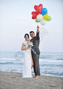 海滩婚礼快乐,刚刚结婚的轻夫妇庆祝,并美丽的海滩日落玩得开心背景