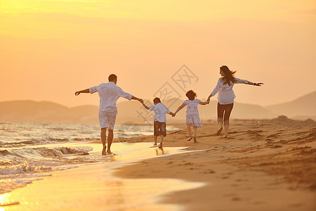 快乐的轻家庭海滩上玩,日落时跑步跳跃图片