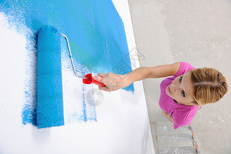 快乐微笑的女人用蓝色绿色的新房子画内墙白色的墙图片