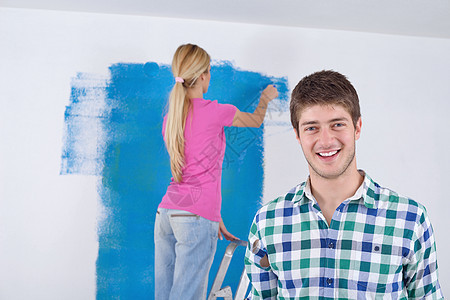 幸福的轻夫妇用绿色蓝色的白色墙壁粉刷他们的新家图片