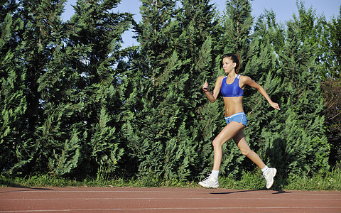 美丽的轻女子日出时体育场的运动跑道上慢跑跑步图片