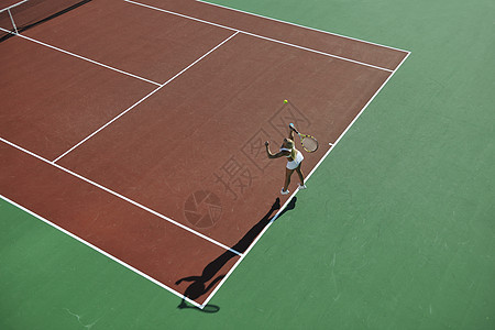 轻健康的女人大早就橙色的网球场上户外打网球图片