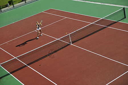 轻健康的女人大早就橙色的网球场上户外打网球高清图片
