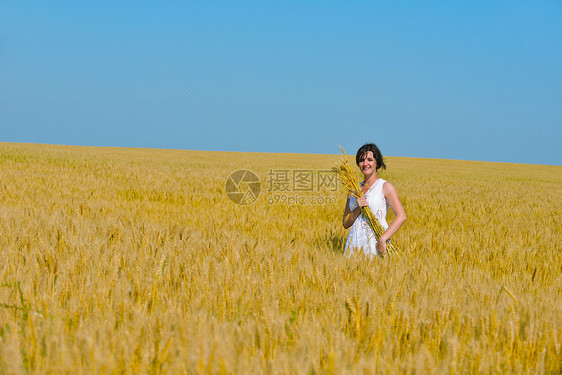 轻女子站蓝天的麦田上跳跃奔跑,夏日的背景代表着健康的生活农业理念图片