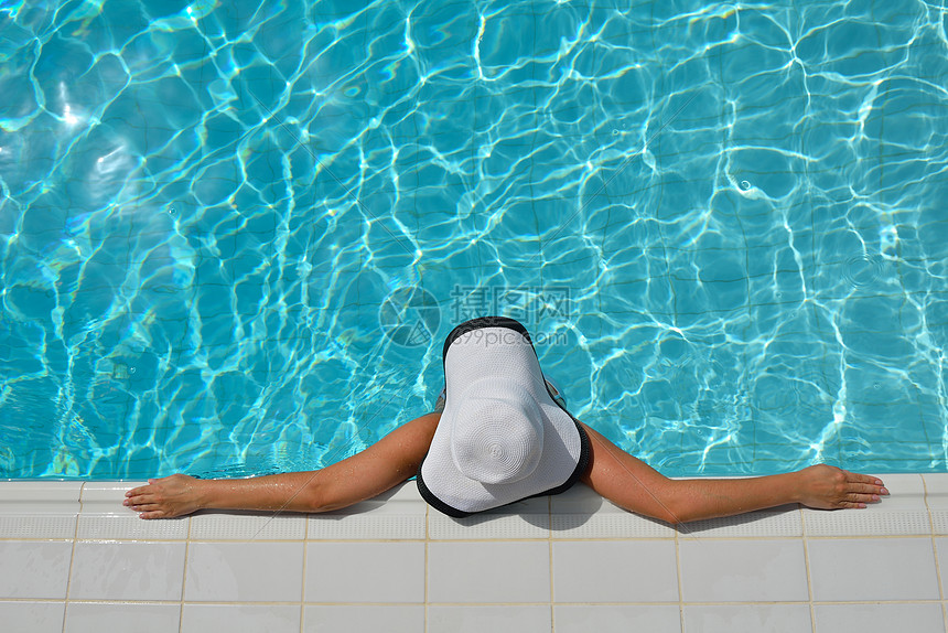 带着帽子太阳镜的快乐微笑的女人热带度假村的游泳池里图片