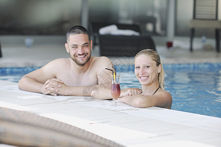 快乐的轻夫妇室内健康游泳池享受快乐的放松喝鸡尾酒图片