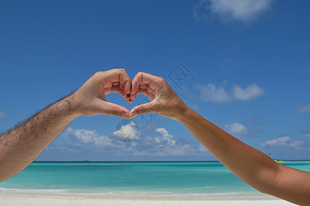 浪漫的情侣阳光明媚的热带海滩背景中的大海上用手臂制作爱情的心形象征图片