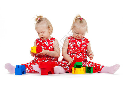 孩子双胞胎的两个相同的双胞胎女孩穿着红色连衣裙玩玩具块图片