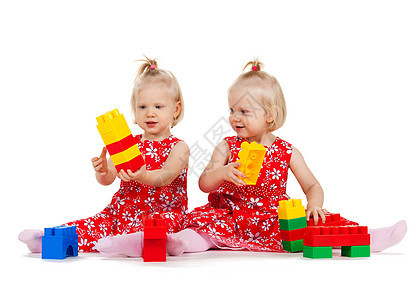 孩子双胞胎的两个相同的双胞胎女孩穿着红色连衣裙玩玩具块图片