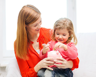 投资商家庭,孩子,金钱,投资家快乐的人的快乐的母亲女儿与小粉红色储蓄罐背景
