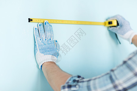 修理建筑家庭用胶带测量墙壁的手套中男的特写图片