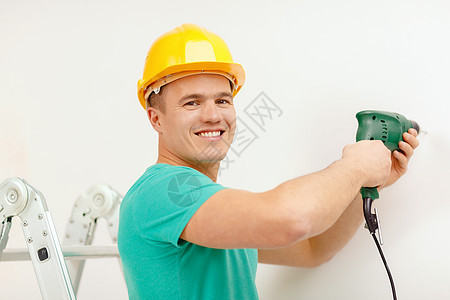 维修,建筑家庭微笑的人黄色防护头盔与电钻墙上制造洞图片
