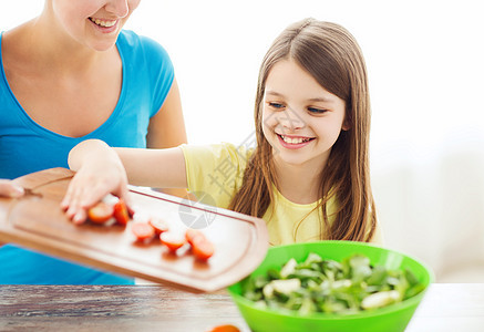 微笑的小女孩母亲厨房的沙拉中添加西红柿图片