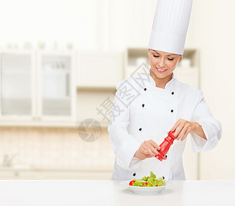 烹饪食物微笑的女厨师准备沙拉与盐胡椒粉磨坊图片