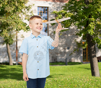 梦想,未来,爱好,教育童的微笑的小男孩手里着木制的飞机模型院子的背景上图片