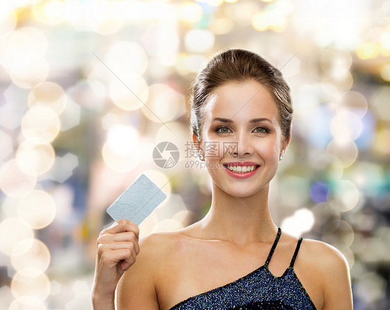 购物,财富,金钱,奢侈品人的微笑的女人穿着晚礼服,假日灯光背景下持信用卡图片