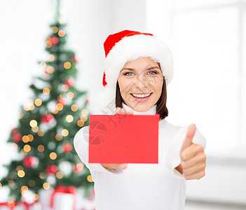 诞节,举行,人,广告销售快乐的女人戴着诞老人助手的帽子,空白的红色卡片,客厅诞树的背景上竖大拇指的手势背景图片