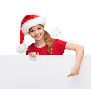 诞节,假日广告快乐的女孩戴着诞老人的帽子,手指指向空白的白板图片