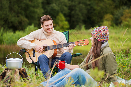 冒险,旅行,旅游人的微笑夫妇与吉他烹饪食物饮酒露营图片