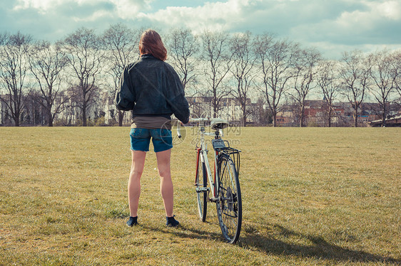 个轻的女人着自行车站公园的草地上图片