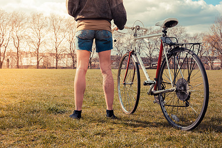 个轻的女人着自行车站公园的草地上图片
