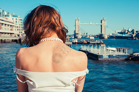 个轻的女人正阳光明媚的日子里晒黑她,看着英国伦敦泰晤士河图片