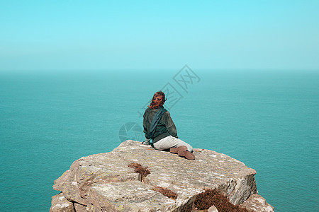轻的女人坐海边的悬崖上图片