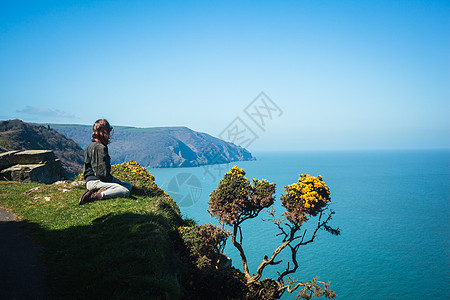 轻的女人坐海边的悬崖边上图片