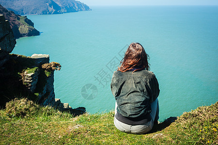 轻的女人坐海边的悬崖边上图片