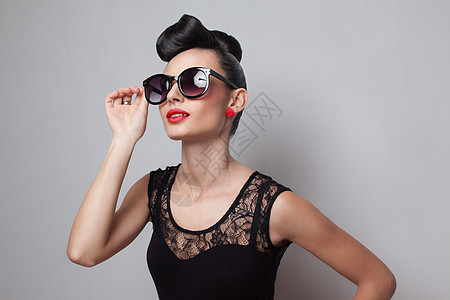 轻时尚的女人戴着圆形太阳镜,穿着华丽的连衣裙红嘴唇向上,扭曲的高髻图片