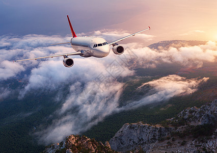 美丽的飞机日落时飞过低云风景与客机,岩石,森林,蓝天与橙色阳光黄昏客机商务旅行商业飞机图片
