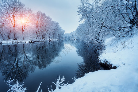 日落时河上的冬季森林五颜六色的风景与雪树,冰冻的河流与倒影水中季节的雪覆盖着树木湖泊太阳蓝天雪冬里美丽图片