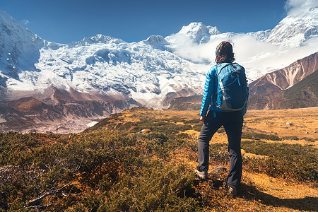石头山谷上的女人站着的轻女人,背着背包石头上,看着雪覆盖的山脉日落风景与女孩,高岩石与雪峰,黄草,蓝天尼泊尔图片