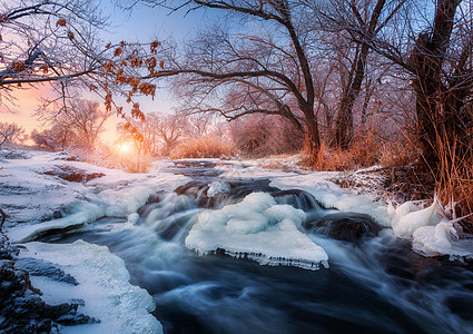 日落时令人惊叹的河流的冬季森林冬天的风景雪树,冰,美丽的冰冻河流,雪丛,黄昏中五颜六色的天空模糊的水小瀑布水图片