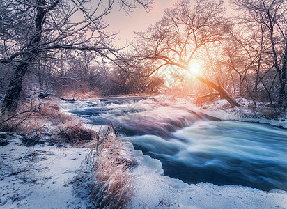 日落时令人惊叹的河流的冬季森林冬天的风景雪树,冰,美丽的冰冻河流,雪丛,黄昏中五颜六色的天空模糊的水小瀑布水背景图片
