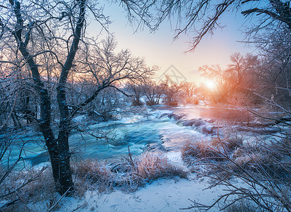 日落时令人惊叹的河流的冬季森林冬天的风景雪树,冰,美丽的冰冻河流,雪丛,黄昏中五颜六色的天空模糊的水小瀑布水图片