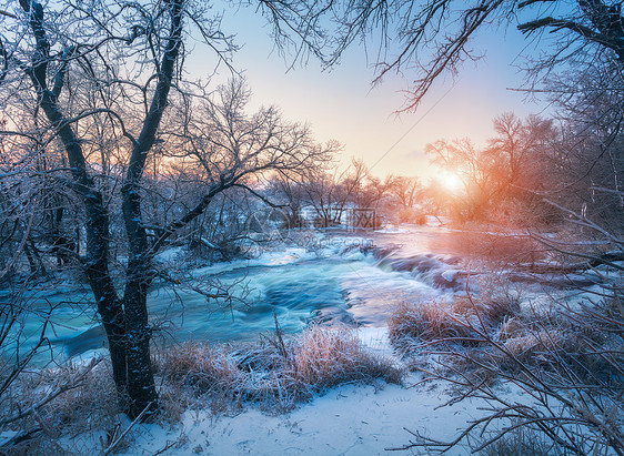日落时令人惊叹的河流的冬季森林冬天的风景雪树,冰,美丽的冰冻河流,雪丛,黄昏中五颜六色的天空模糊的水小瀑布水图片