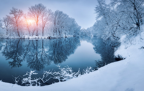 日落时河上的冬季森林五颜六色的风景与雪树,河流与倒影寒冷的夜晚雪覆盖着树木湖泊太阳蓝天雪冬里美丽的森林冬图片