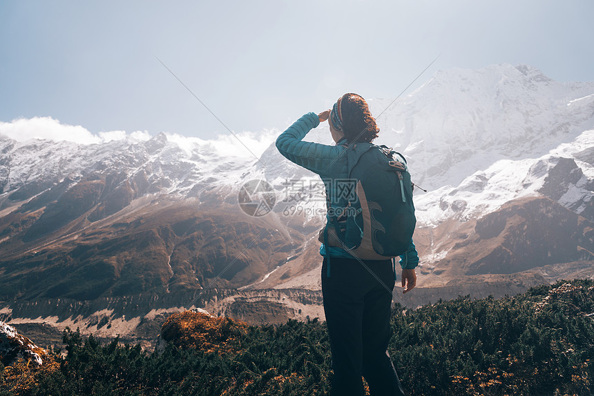 女人带着背包日出时看着美丽的云山风景与女孩,高岩石与雪峰,蓝天与云尼泊尔旅行旅游复古风格自然图片