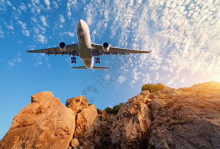 大白色飞机日落时飞过岩石风景与客机,山,彩色蓝天与云客机正降落商务旅行商业飞机图片