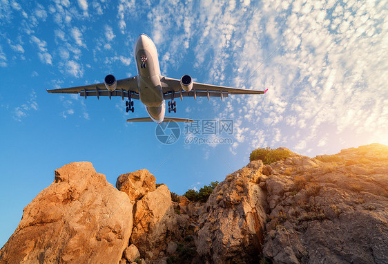 大白色飞机日落时飞过岩石风景与客机,山,彩色蓝天与云客机正降落商务旅行商业飞机图片