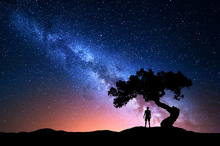 银河系夜空中星星,老树个独自站山上的人的轮廓银河带着红光人山上星系树下个人的剪影宇宙图片