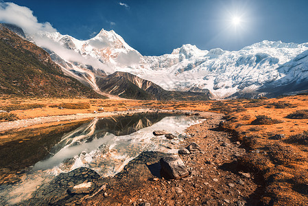 美丽的景色高高的岩石,雪覆盖着山峰,山湖里的石头,水中的倒影,日落时的蓝天尼泊尔美丽的风景与喜马拉雅山脉明亮的晴天图片