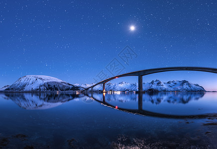 神奇的桥星空,美丽的倒影水中夜风景与桥,雪山,蓝天与月亮明亮的星星反射海上挪威洛福滕岛的冬天图片