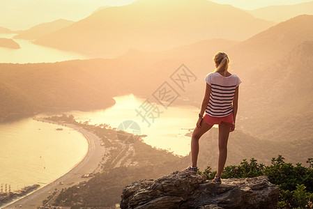 轻的女人站岩石的顶端,看着海滩山脉,夏天五颜六色的日落风景与女孩,海洋,山脊橙色的阳光旅行奥卢德尼斯,火鸡图片