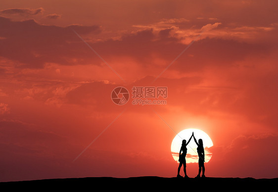 个站立的轻运动女孩的剪影个站立的轻运动女孩的剪影,举手臂山上太阳红色的天空与云的背景风景与妇女牵手五颜六图片