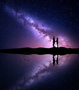 银河里人的轮廓夜空的景观银河里人的轮廓夜空的景观,男人女人牵着手湖边的山上,水中倒影拥抱银河夫妇宇图片