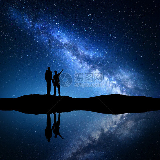 银河系的景观父子的剪影银河系个家庭的轮廓父亲个儿子指着夜空河边的山上,天空水中反射夜风景图片